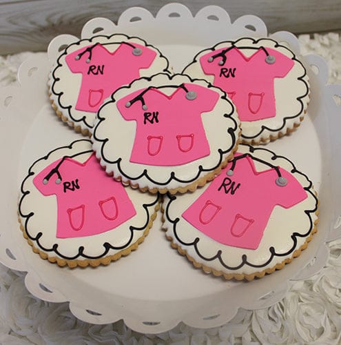 CE-006b graduation round cookies with white icing and a pink nurse scrub top design featuring "RN" and a small stethoscope, arranged on a white scalloped platter.