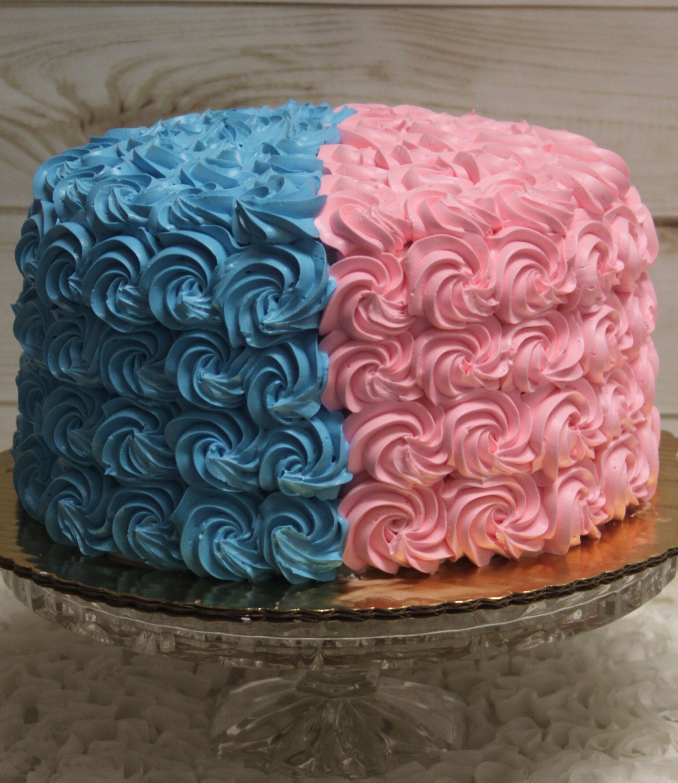 The CB-125 is a round cake with blue rosettes on the left half and pink rosettes on the right half, displayed on a glass cake stand.