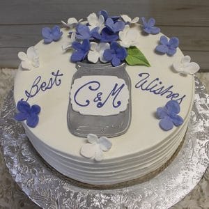 The BR-027 is a round cake with white frosting, topped with purple and white flower-shaped fondant and a mason jar design featuring "C & M" in the center. "Best Wishes" is written in purple icing.