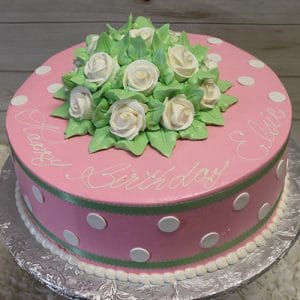 BD-159 is a pink birthday cake with white polka dots, green trim, and white icing roses on top. "Happy Birthday Ellie" is written in white icing, and the cake is displayed on a silver platter.