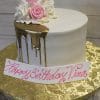 The BD-057C Gold Drip Partial is a white cake with gold drip icing, pink and white icing roses on top, on a gold floral-patterned board. A "Happy Birthday Tina" sign in pink script sits in front.