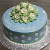 A round blue BD-160 cake with white polka dots, green trim, and "Happy Birthday Maureen" in white icing. Topped with white icing roses and leaves, it sits on a silver foil-covered board.