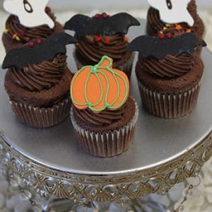 Five CC-053 Mini Halloween cupcakes—chocolate with white mousse filling—are topped with festive decorations and displayed on an ornate silver cake stand.