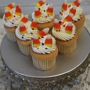 Six CC-055 Mini Halloween cupcakes with gold color and chocolate mousse filling sit on a decorative silver cake stand against a textured white background.