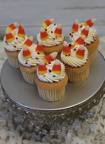 Six CC-055 Mini Halloween cupcakes with gold color and chocolate mousse filling sit on a decorative silver cake stand against a textured white background.