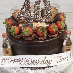 The BD-024D ChocolateTitos features a chocolate cake topped with chocolate-covered strawberries, mini Tito’s vodka bottles, and a large chocolate 40 topper. A white banner at the base says “Happy Birthday Tim!” in cursive.