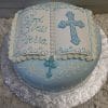 The RC-096 is a round cake designed as an open book with blue and white icing, a cross, and "God Bless Cierra" written on one page. It sits on a silver floral-patterned board.