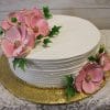 The BR-019 cake is round and white with frosted horizontal textured sides, decorated with large pink sugar flowers, green leaves, a gold pearl border, and set on a gold cake board.