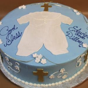 Product RC-037: Round blue cake topped with white fondant baby outfit, gold crosses, small white flowers, and blue "God Bless Edwin and Dillon" text. Presented on a silver board.