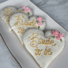 The CE-003e bridal set features three heart-shaped cookies with white icing, gold sparkles, yellow "Bride to be" lettering, and pink icing roses, arranged on a rectangular white plate.