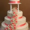 WC-047 is a three-tier white wedding cake featuring pink ribbon accents, cascading white and pink roses, and a cluster of roses on the top tier.