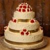 The WC-031 is a three-tiered white wedding cake with intricate icing, gold ribbon bands on each layer, and red and white rose toppers, displayed on a silver base.