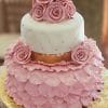 The WD-081 is a two-tiered cake with pink and white fondant, adorned with pink fondant roses on top. Pink petal layers cover the bottom tier, and a gold ribbon separates the tiers. It is presented on a gold board.