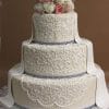 The WD-177 is a three-tiered white wedding cake featuring lace-like icing, topped with white and pink roses, and finished with elegant white fondant ribbons cascading down the sides.