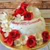 The BD-054D red quilted is a white, dome-shaped cake with red roses, white flowers, and gold pearls, featuring “Happy 25th Anniversary” in red icing. It’s displayed on a gold board with a wooden background.