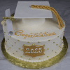 The GC-0006 is a round white graduation cake featuring a gold "2025" plaque, gold beads, a diploma, and a white cap with a gold tassel. "Congratulations" is written in gold icing on top.