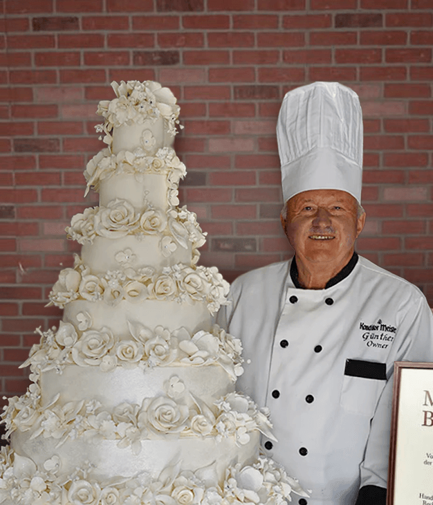 Gunther of Konditor Meister standing beside an ornate multi-tier white wedding cake