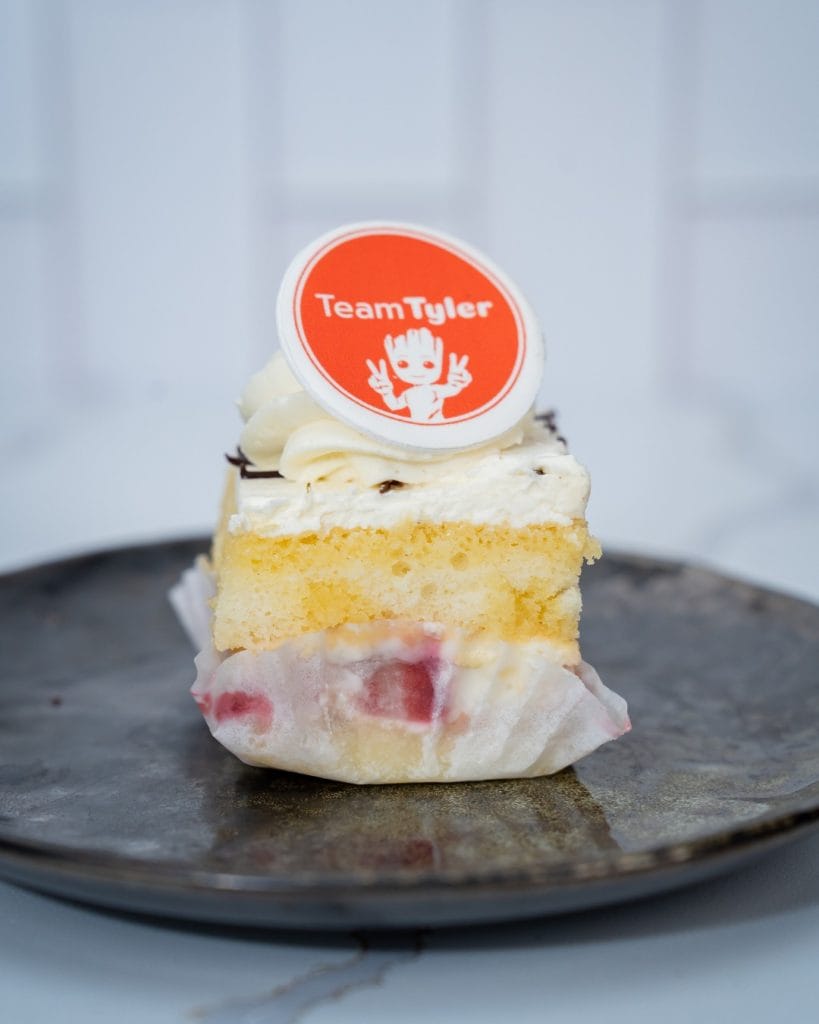 Vanilla cake slice with strawberry filling, buttercream frosting, and a Team Tyler edible logo topper