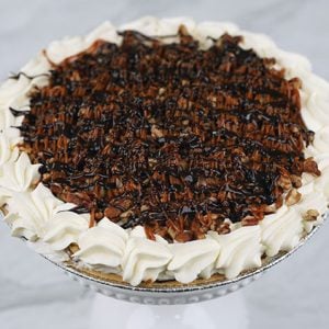 Turtle pie topped with chocolate drizzle, caramel, and chopped pecans with whipped cream border