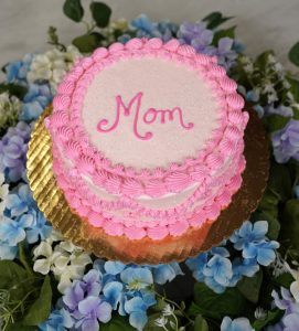 cake petite One Size features pale pink frosting, a pink “Mom” written on the top with a brighter pink piping along the top and bottom edge.