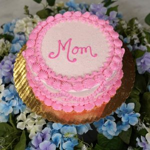 cake petite One Size features pale pink frosting, a pink “Mom” written on the top with a brighter pink piping along the top and bottom edge.