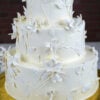 WD-106 is a three-tier white wedding cake featuring delicate botanical details with sculpted white flowers, leaves, and flowing vines. The monochromatic design creates an elegant and modern floral look.
