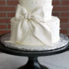 WD-108 is a two-tier white wedding cake decorated with pearl accents and an oversized white bow wrapped around the tiers.
