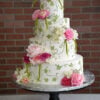 WD-112 is a four-tier white wedding cake decorated with green vine details and cascading pink, white, and fuchsia flowers.