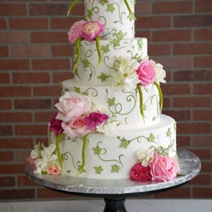 WD-112 is a four-tier white wedding cake decorated with green vine details and cascading pink, white, and fuchsia flowers.
